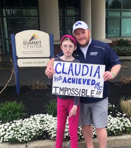 Claudia Rosenecker, and her dad, Tom, pose in front of The Summit Center with a sign that reads, "Claudia achieved the impossible."